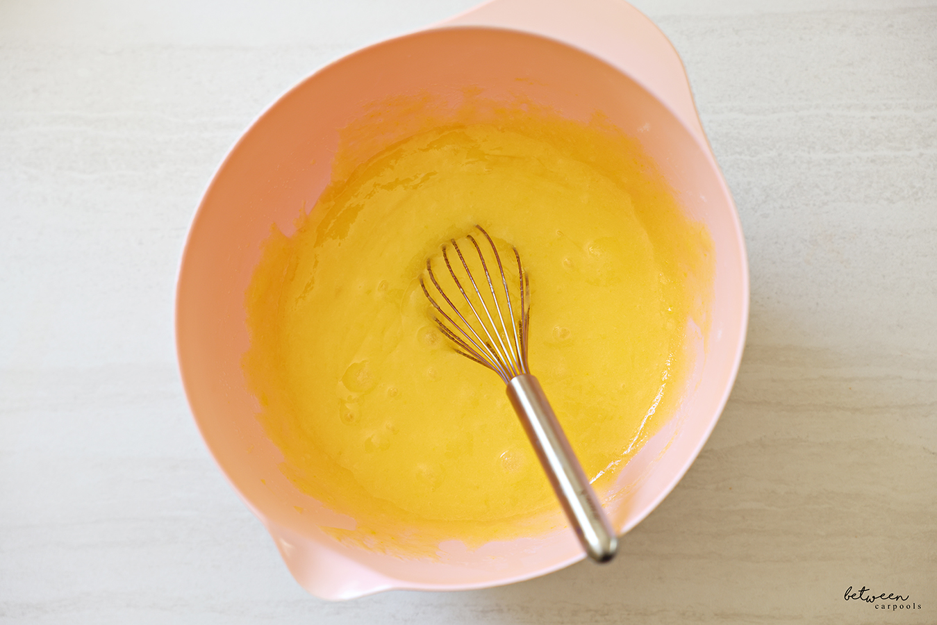 Sugar, oil, and eggs, whisked together in a pink mixing bowl with spout with a whisk.