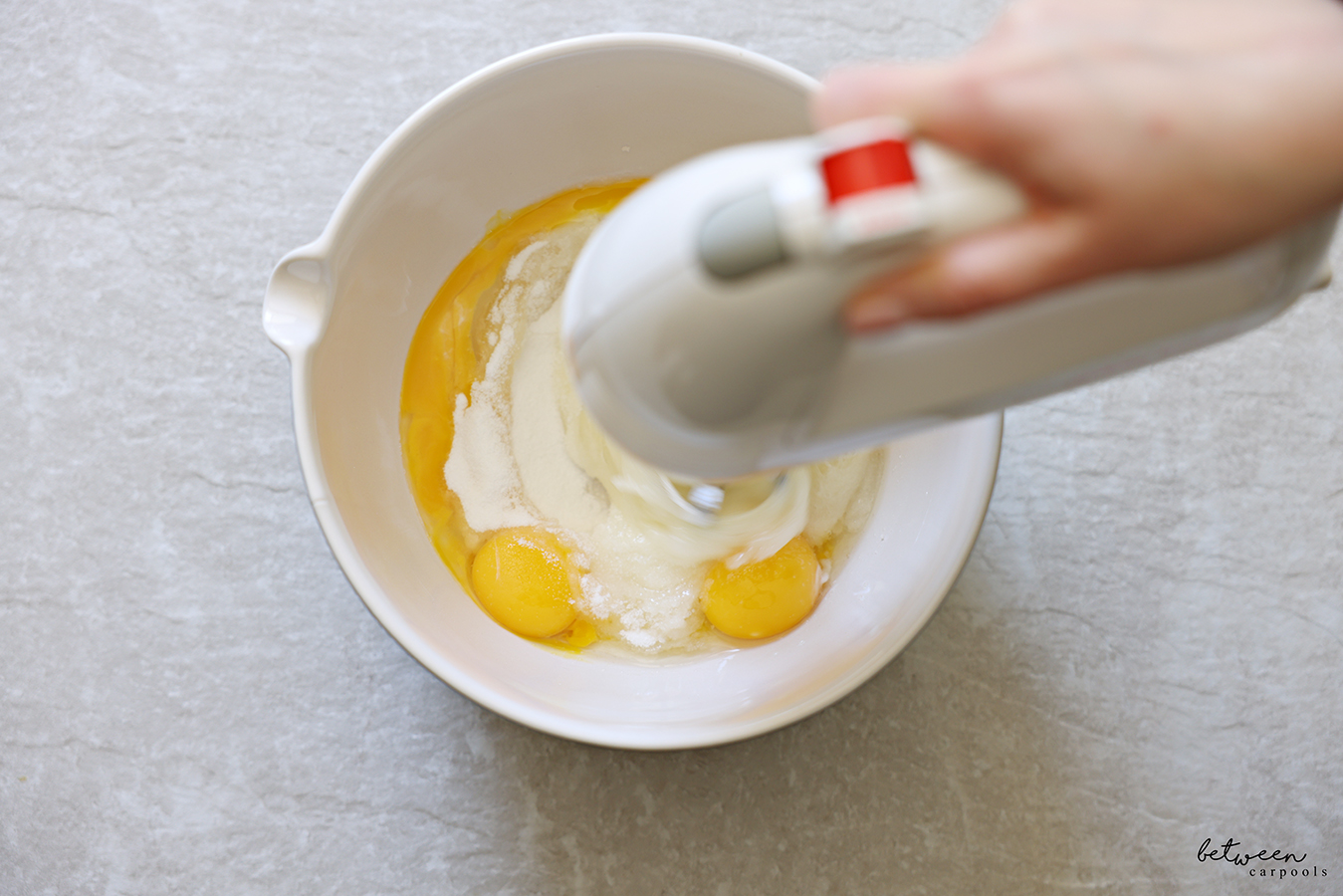 Beating eggs and sugar in a mixing bowl with spout with a hand mixer.