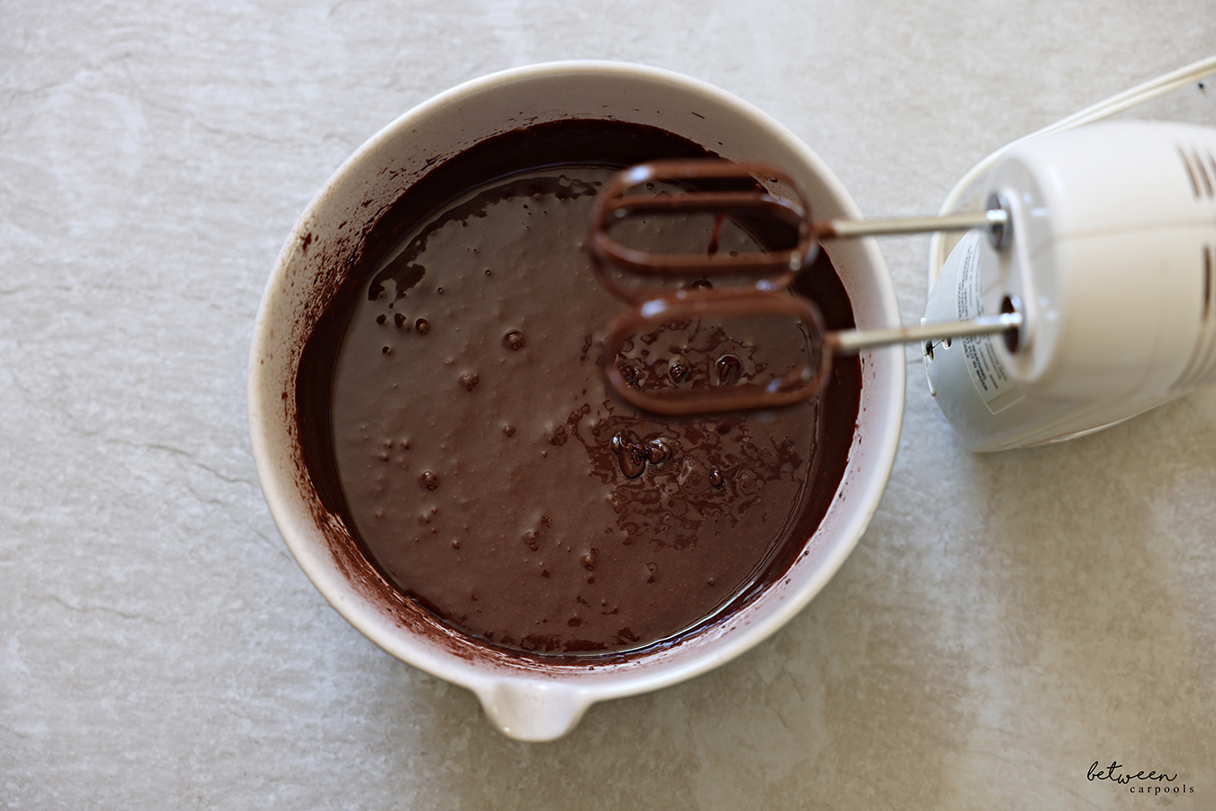 Chocolate muffin batter in a mixing bowl with spout. Hand Mixer beaters leaning on the bowl rim.