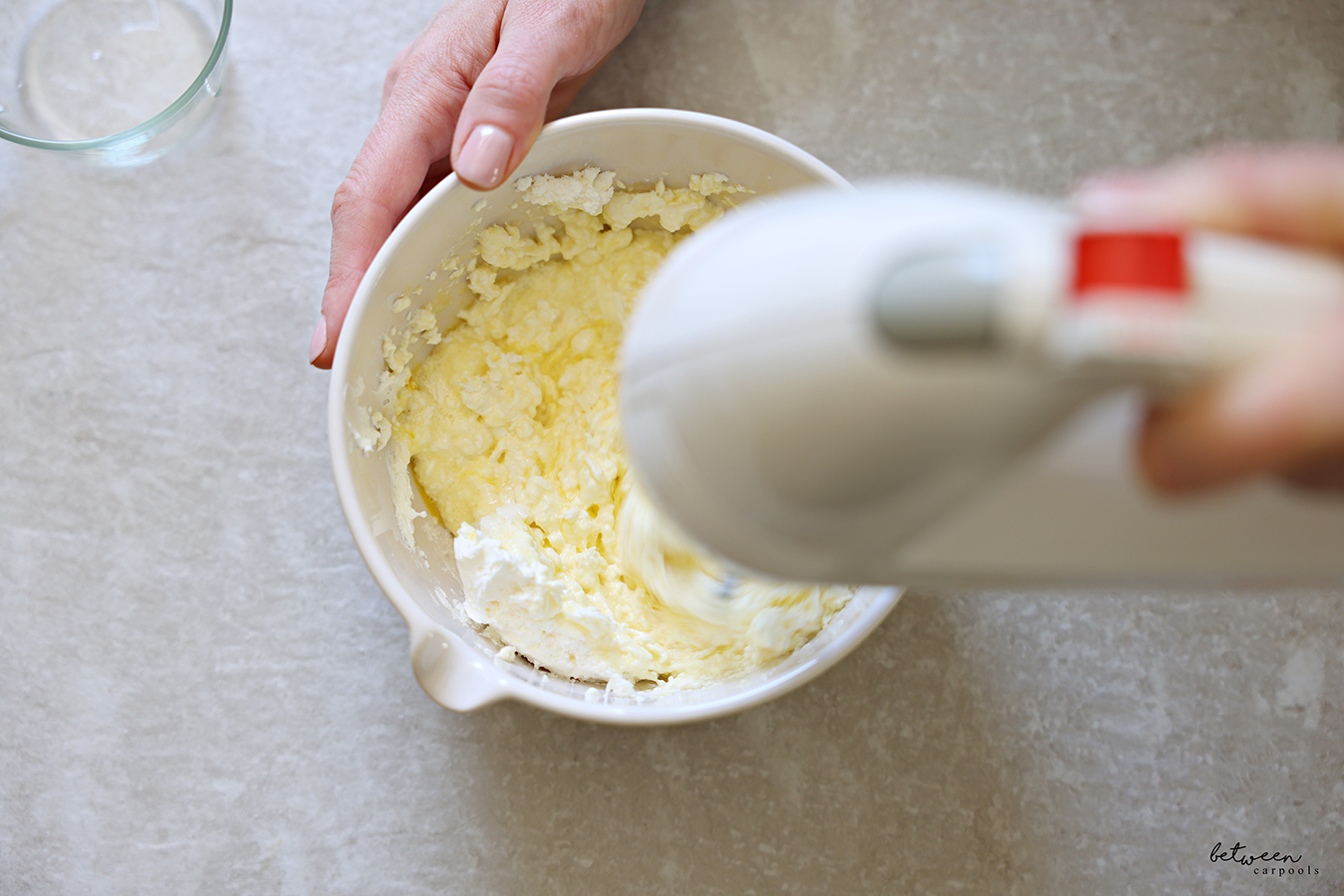 Blending cream cheese, sugar, and egg in a mixing bowl with spout with a hand mixer.