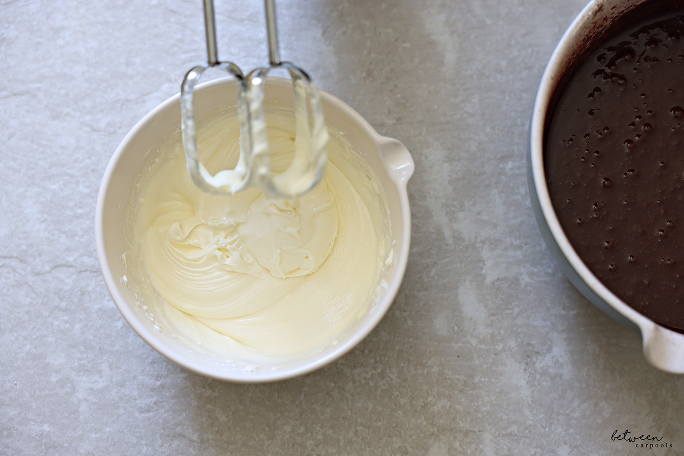 Creamy cheese mixture and chocolate muffin batter in bowls with spouts. Hand Mixer beaters leaning on the cheese mixture bowl rim.