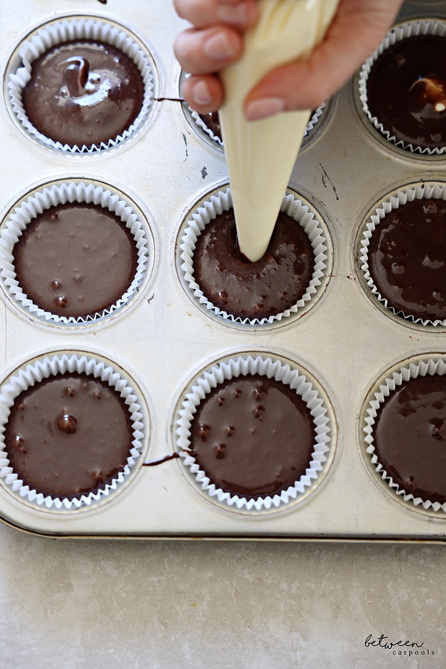 Piping cheese mixture into muffin cups with chocolate batter.