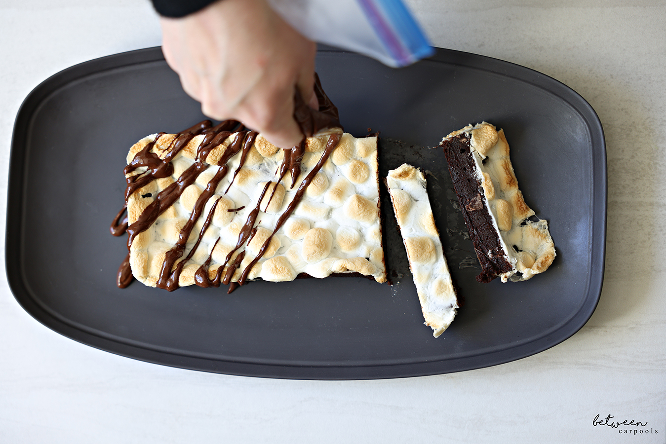 Drizzling Almond Butter Ganache topping on a Rocky Road Marshmallow Brownie loaf on a platter.