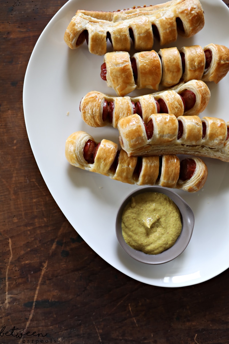 pull apart hot dogs, baked, on a white oval tray with mustard in a stainless condiment bowl