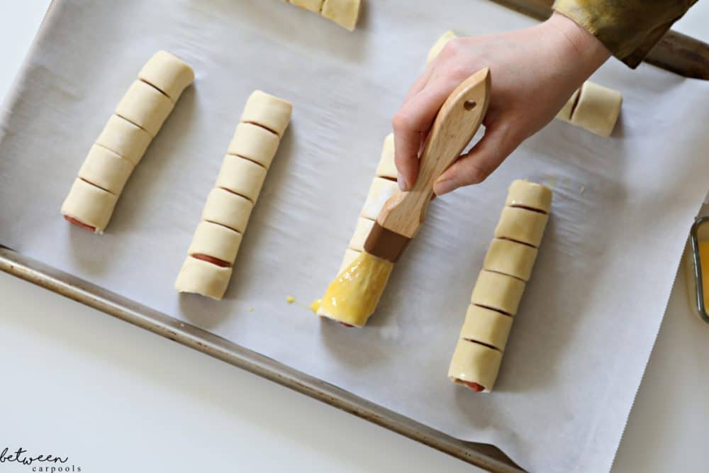 egging pull apart hot dogs on a parchment lined baking sheet ready to go into the oven