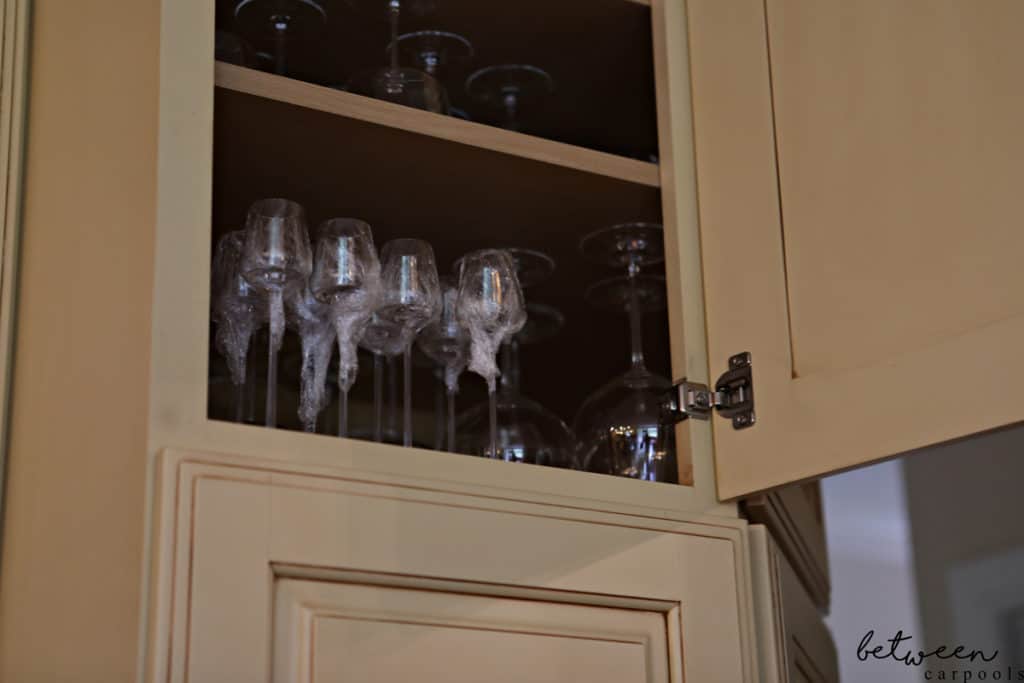 Stemware on a kitchen cabinet shelf - tops covered with Saran Wrap