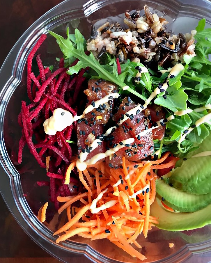 A close-up of an assembled poke bowl in a plastic salad bowl.