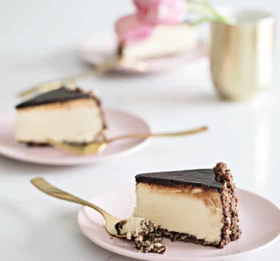 Slices of Coffee Crunch Cheesecake on blush pink dessert plates with gold forks