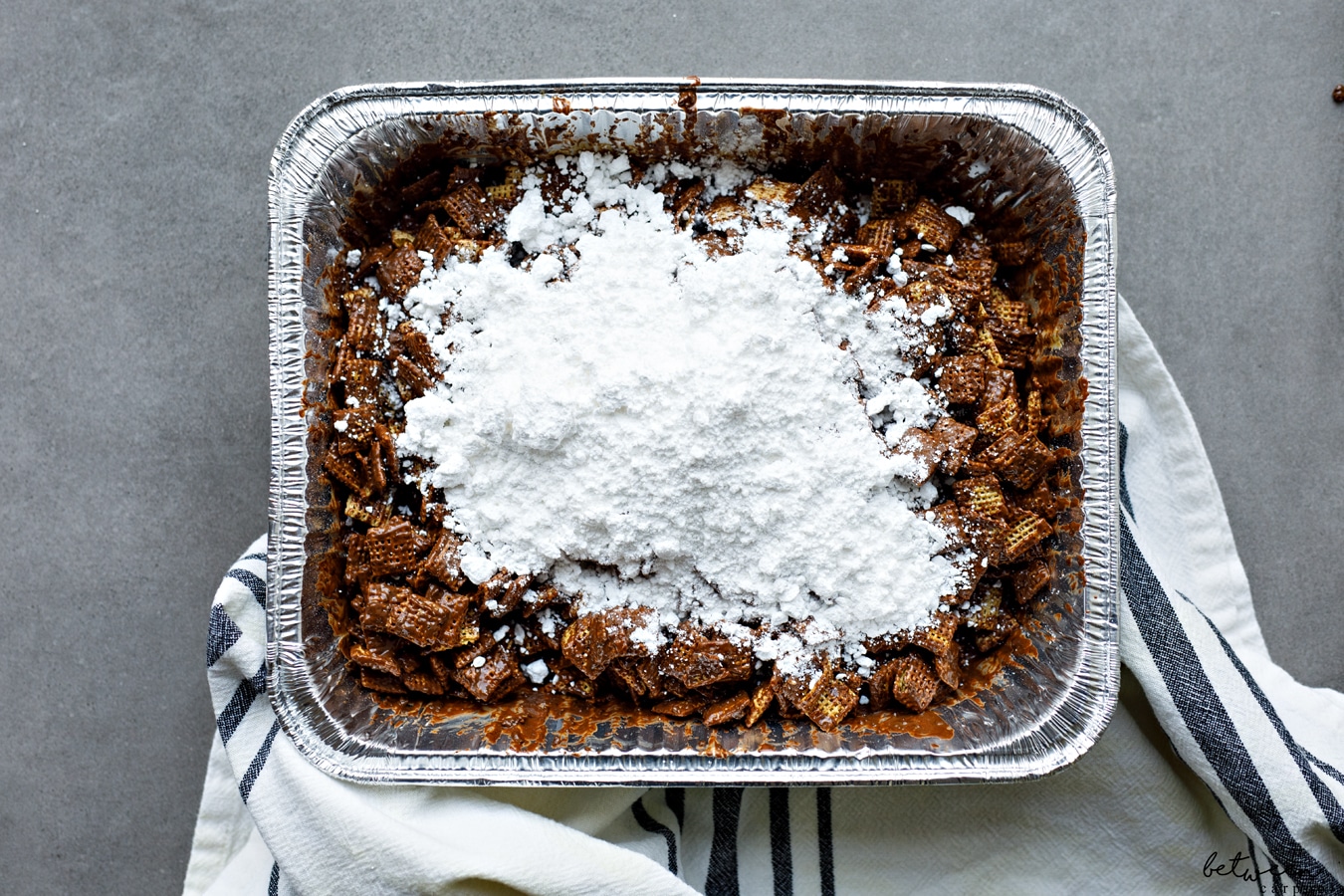 Confectioners sugar on combined muddy buddies in a 9x13 pan.