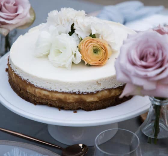 Classic New York Cheesecake on a white cake stand with fresh flowers on the center of the cake