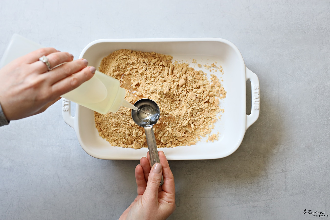 Adding oil to crushed graham crackers in a 9x13 pan.