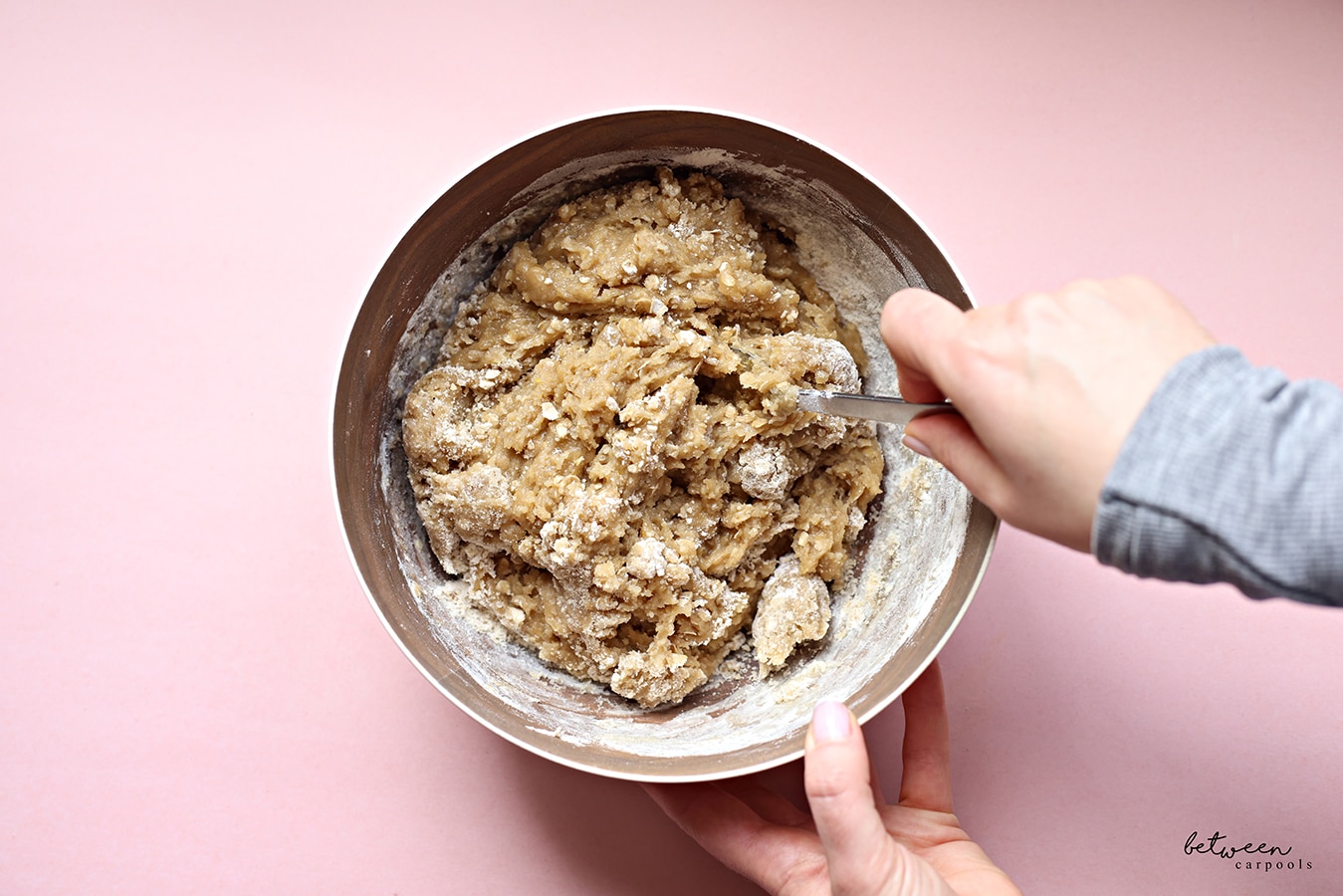 Mixing all ingredients for chocolate chip cookies in a metal mixing bowl with a fork.