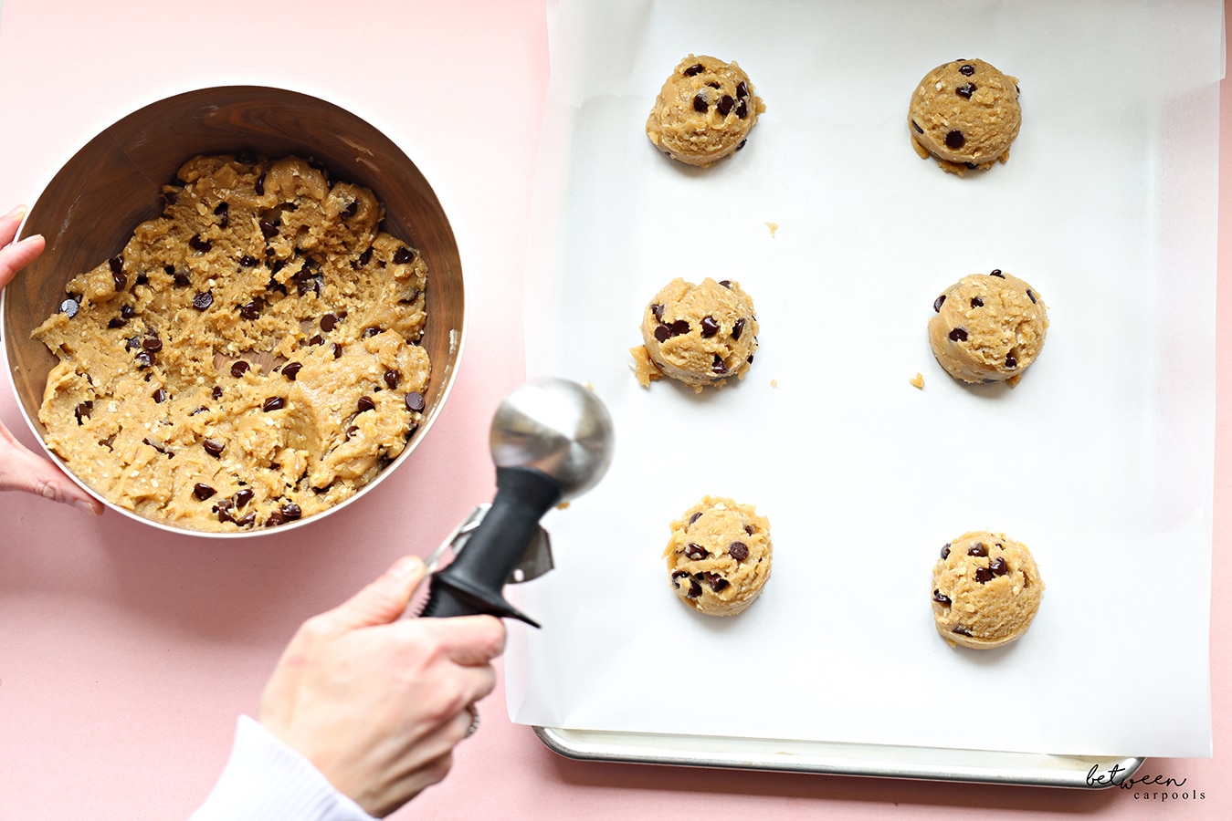 Scooping chocolate chip cookie dough onto a metal sheet pan lined with parchment paper.