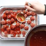 Adding sauce to raw meatballs in a 9x13 pan.