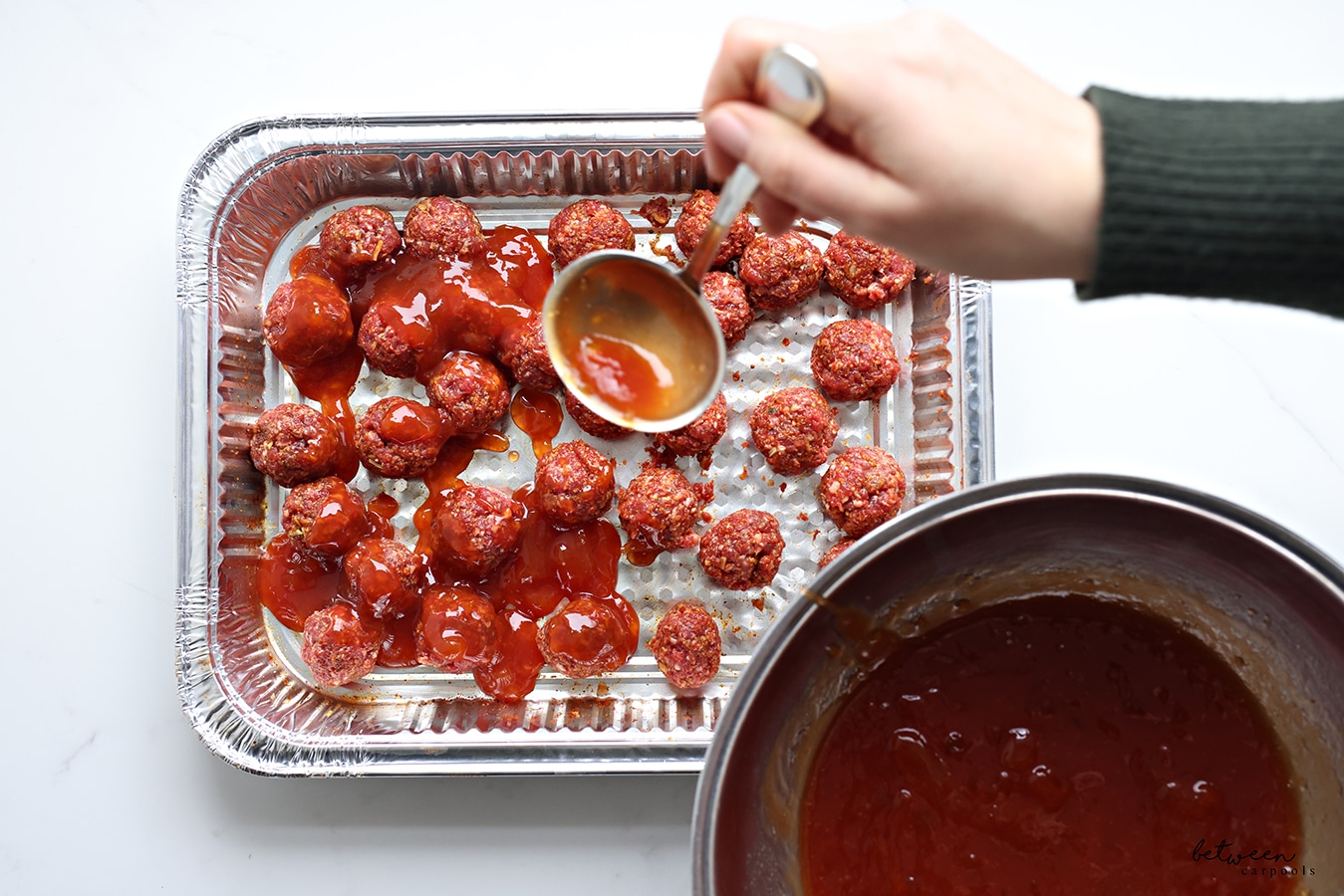 Adding sauce to raw meatballs in a 9x13 pan.