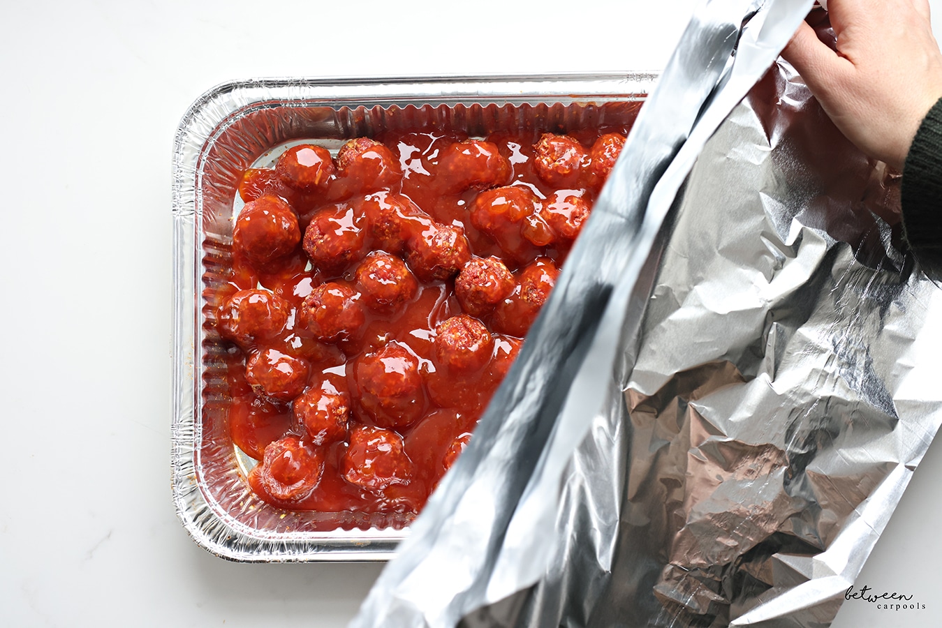 Covering a pan of raw meatballs ready to bake.