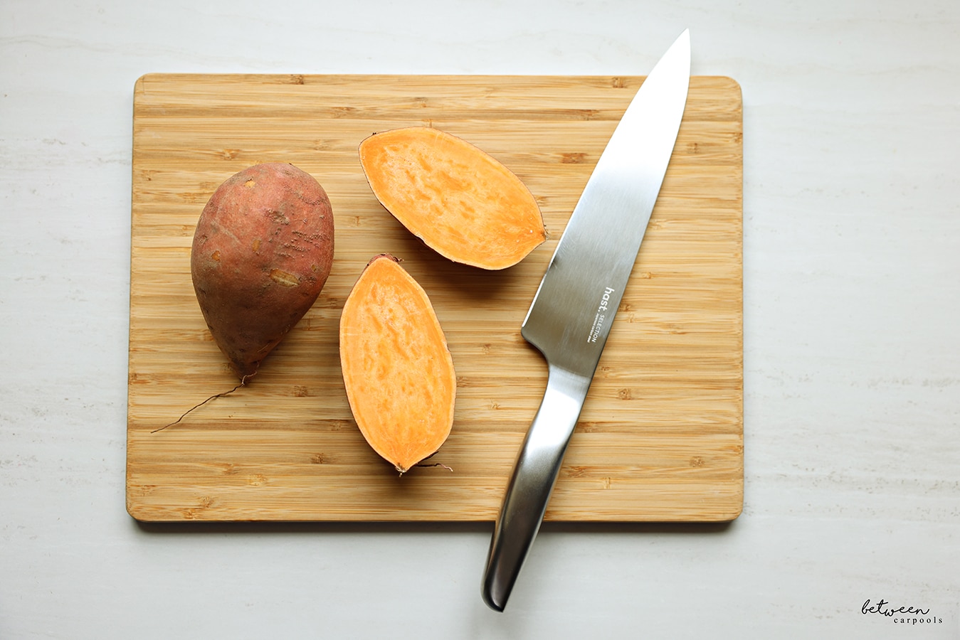 hast chef knife on a cutting board with 2 sweet potatoes, one potato in half
