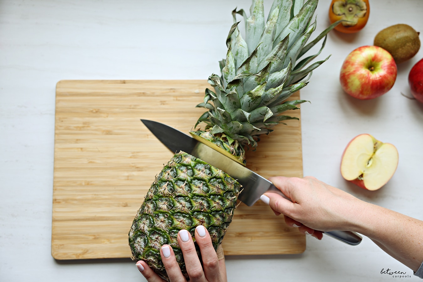 hast chef knife cutting the top of a pineapple off, on a cutting board