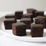 Glazed squares of chocolate cake on a white platter.