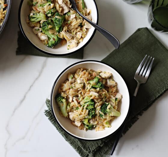 Plated Orzo and Chicken Stir-Fry in bowls with dinner forks on hunter green fringed cloth napkins. Marble background