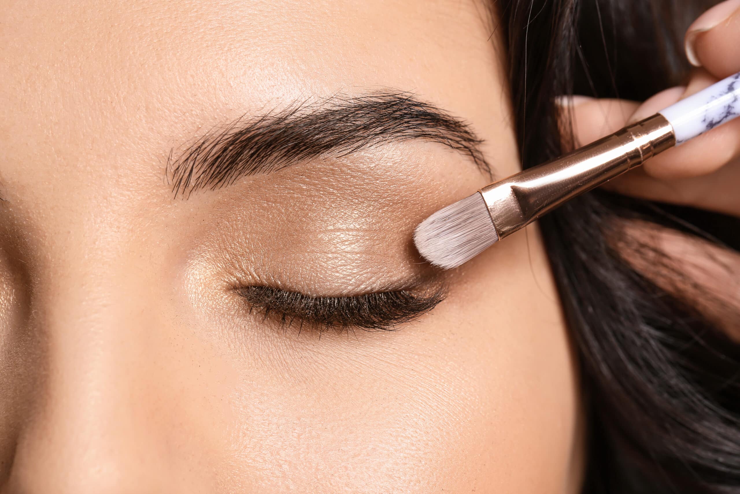 Beautiful young woman applying eyeshadow, closeup