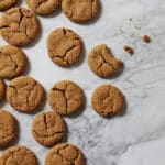 baked gingersnap cookies. one bitten into. crumbs. on marble countertop. top view image