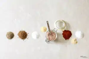 all purpose coffee spice rub in an open clamp lid glass mason jar with a 1 tsp. measuring spoon, and small piles of each ingredient on stone countertop
