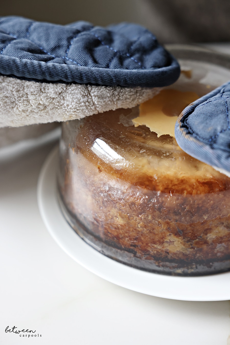 potato kugel in round pyrex flipped onto a white dinner plate using oven mits