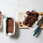 3 baked fudgy chocolate cakes in loaf pans. one is sliced on parchment paper on a cutting board with a knife