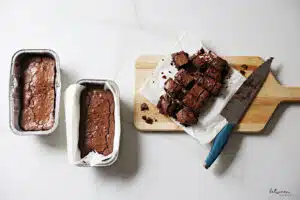 3 baked fudgy chocolate cakes in loaf pans. one is sliced on parchment paper on a cutting board with a knife