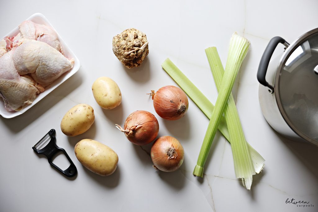 Chicken, golden potatoes, celery stalks, celery knob, onions, a peeler and an 8 quart pot.
