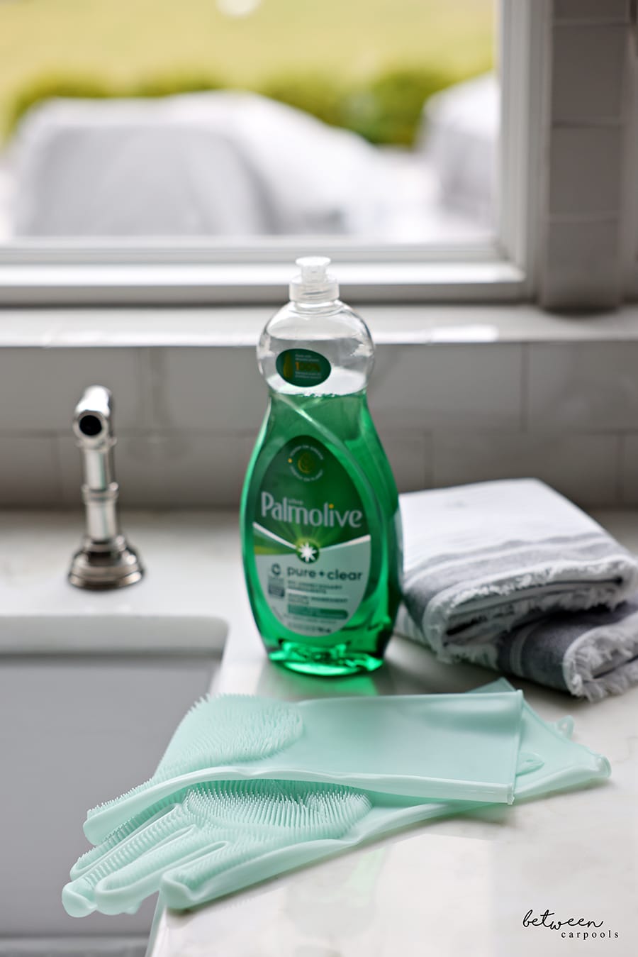 closeup of dish soap, dish cloths and gloves on the counter, at the edge of kitchen sink