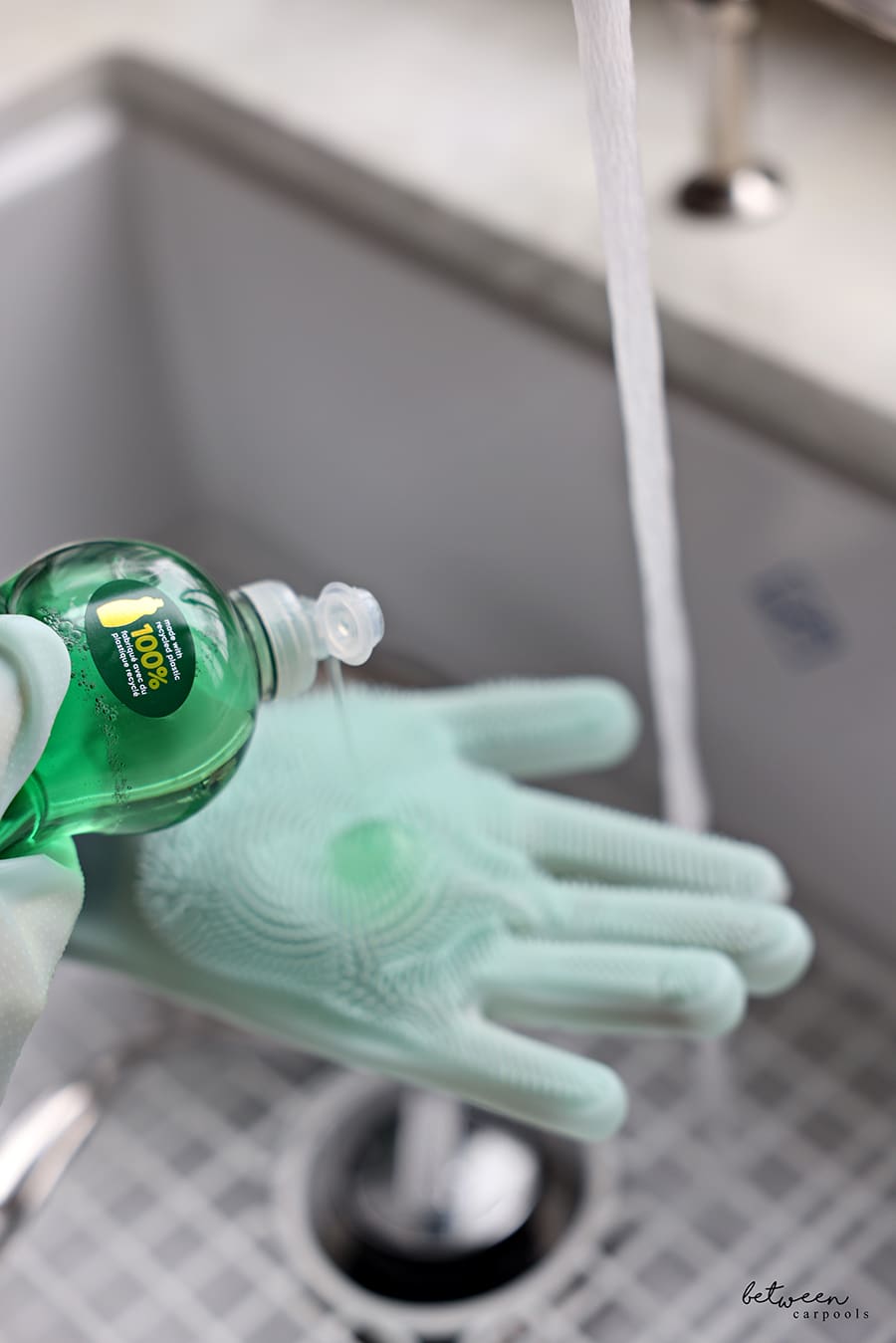 pouring dish soap on the gloves. water running in kitchen sink