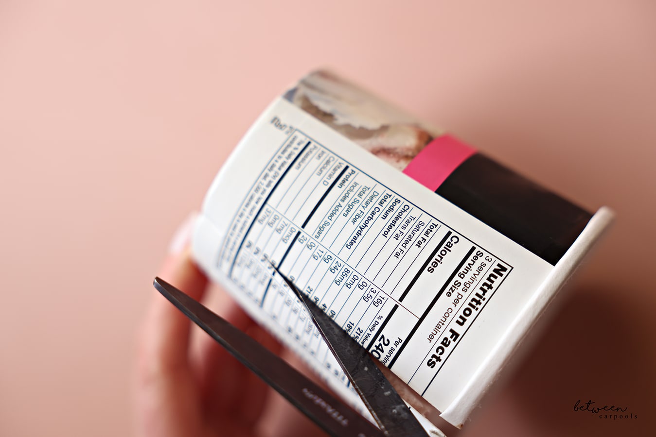 one pint of ice cream. on its side, slicing the cardboard with a scissor