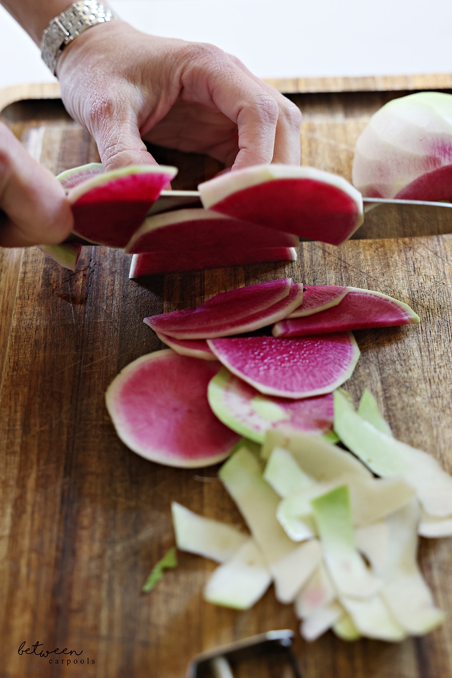 thinly slicing half rounds of watermelon radish on a wooden cutting board