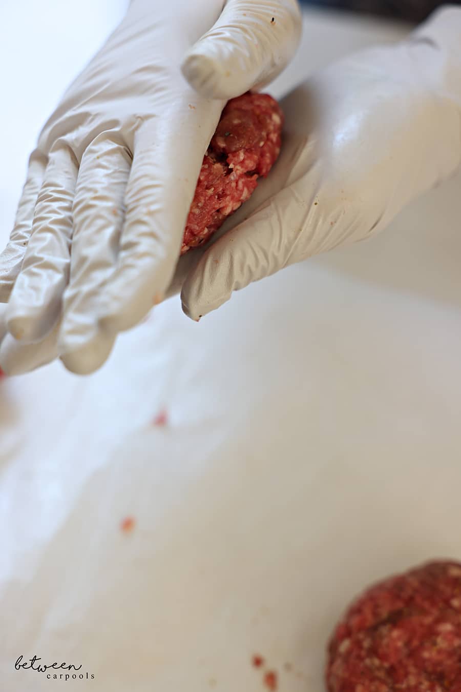 flattening a ball of ground beef mixture between both (gloved) hands