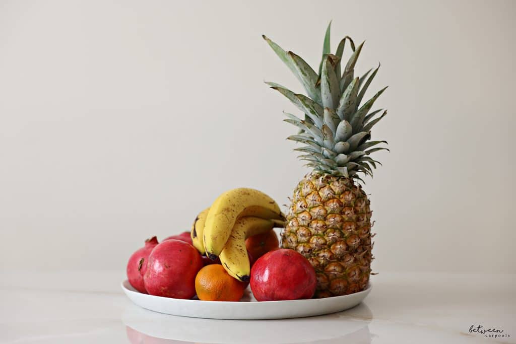 Whole fruit on a white platter. Pineapple, bananas, pomegranates, clementine
