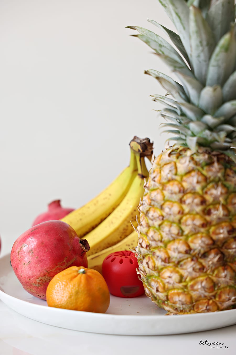 Whole fruit on a white platter. Pineapple, bananas, pomegranates, clementine
