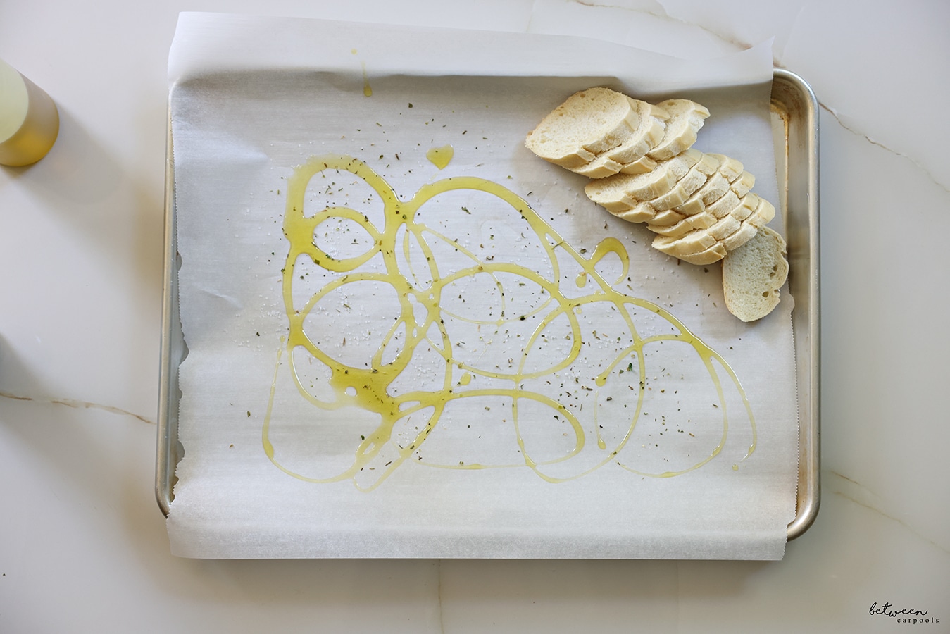 sliced baguette on parchment lined baking sheet with olive oil drizzled on the parchment