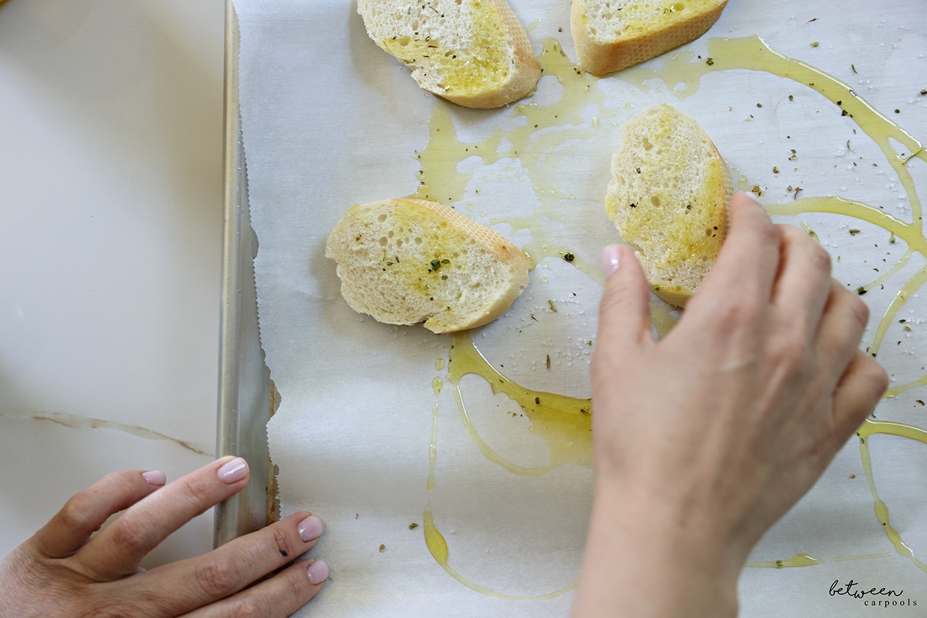 dipping sliced baguette into oil and seasoning on a parchment lined baking sheet