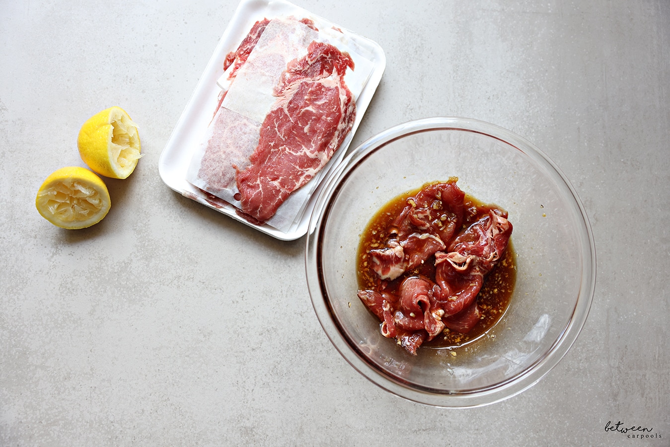 thinly sliced ribeye in butcher packaging and some in the marinade in a glass mixing bowl
