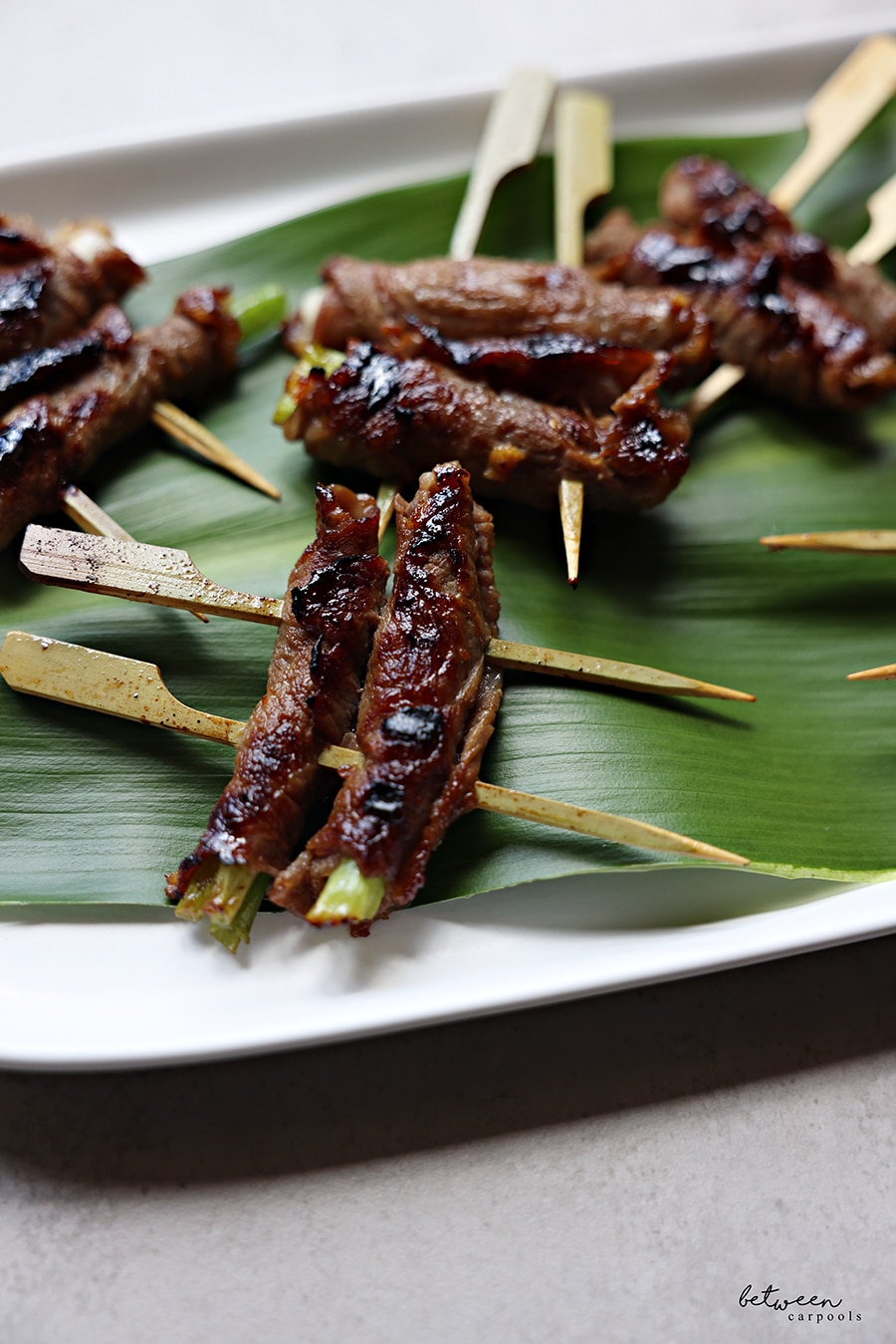 grilled roll ups on a banana leaf on a white oval platter