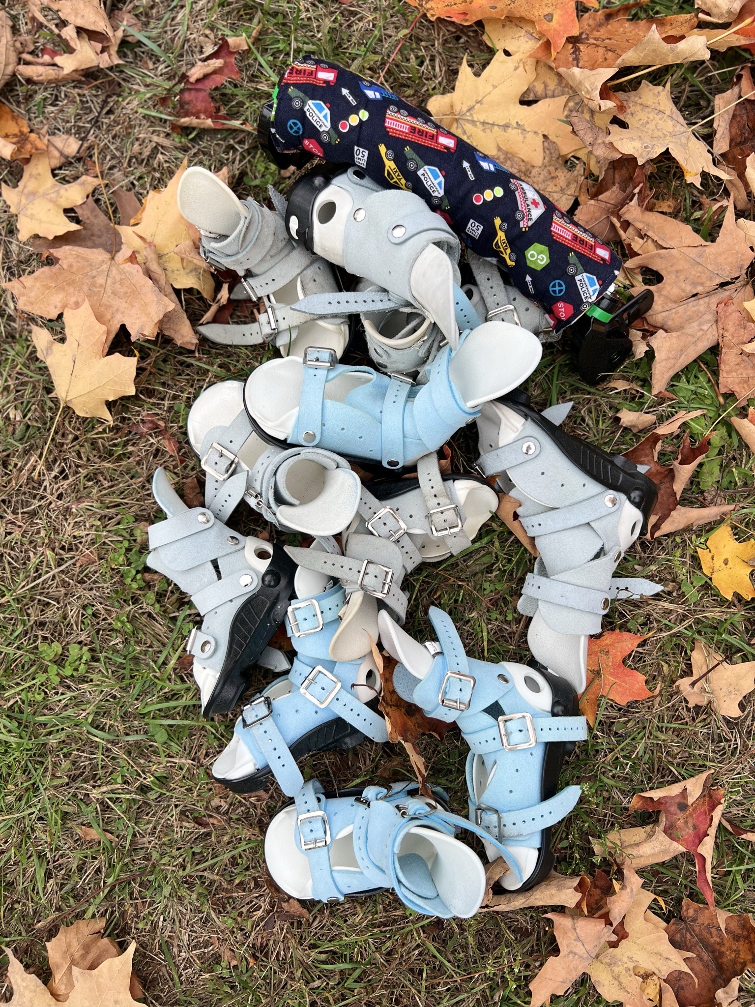 a pile of clubfoot paraphernalia on leafy grass outdoors. boots and bar
