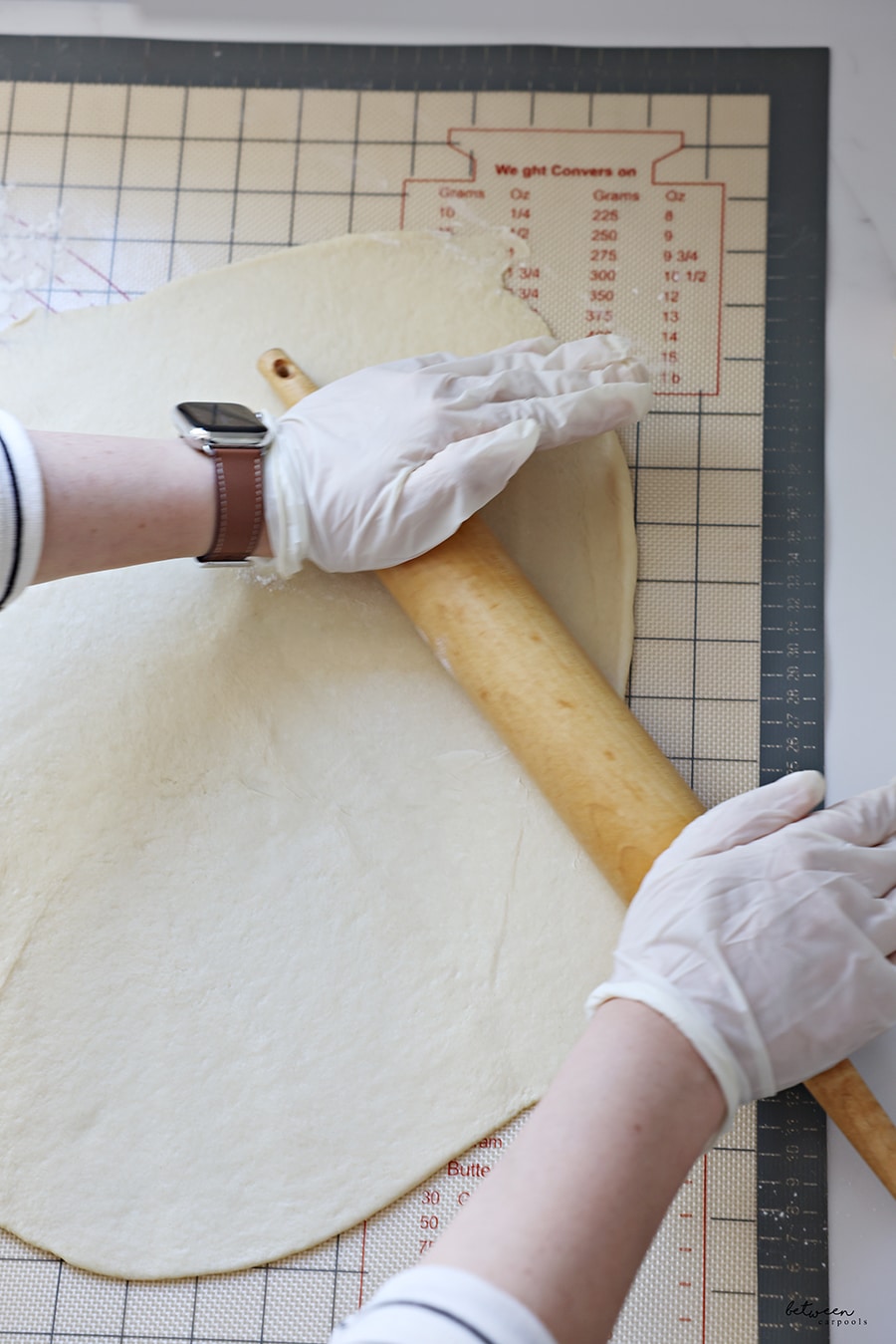 rolling kokosh cake dough with gloved hands and a rolling pin on a baking mat