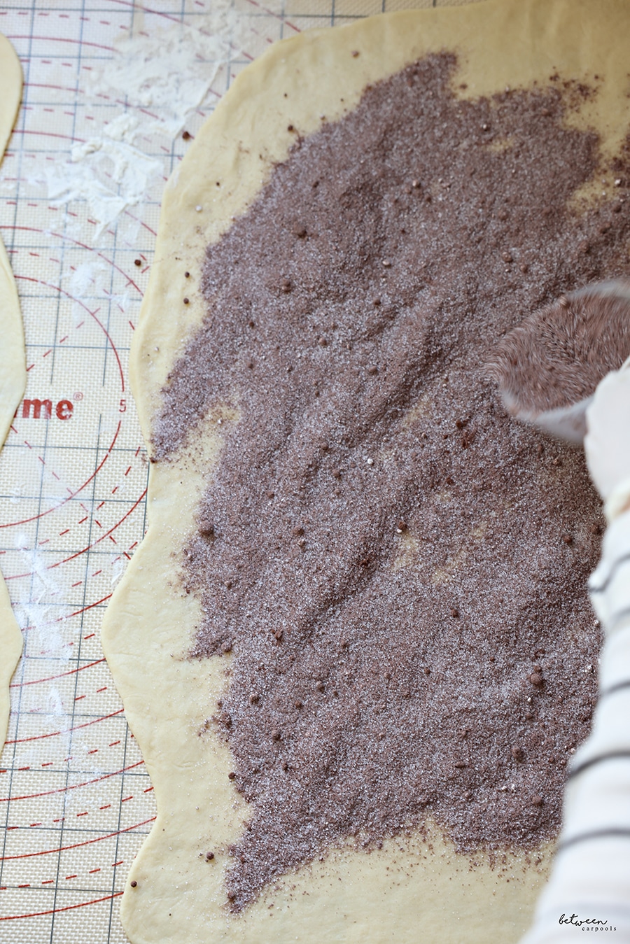 sprinkling cocoa onto rolled out kokosh cake dough on a baking mat, with gloved hands