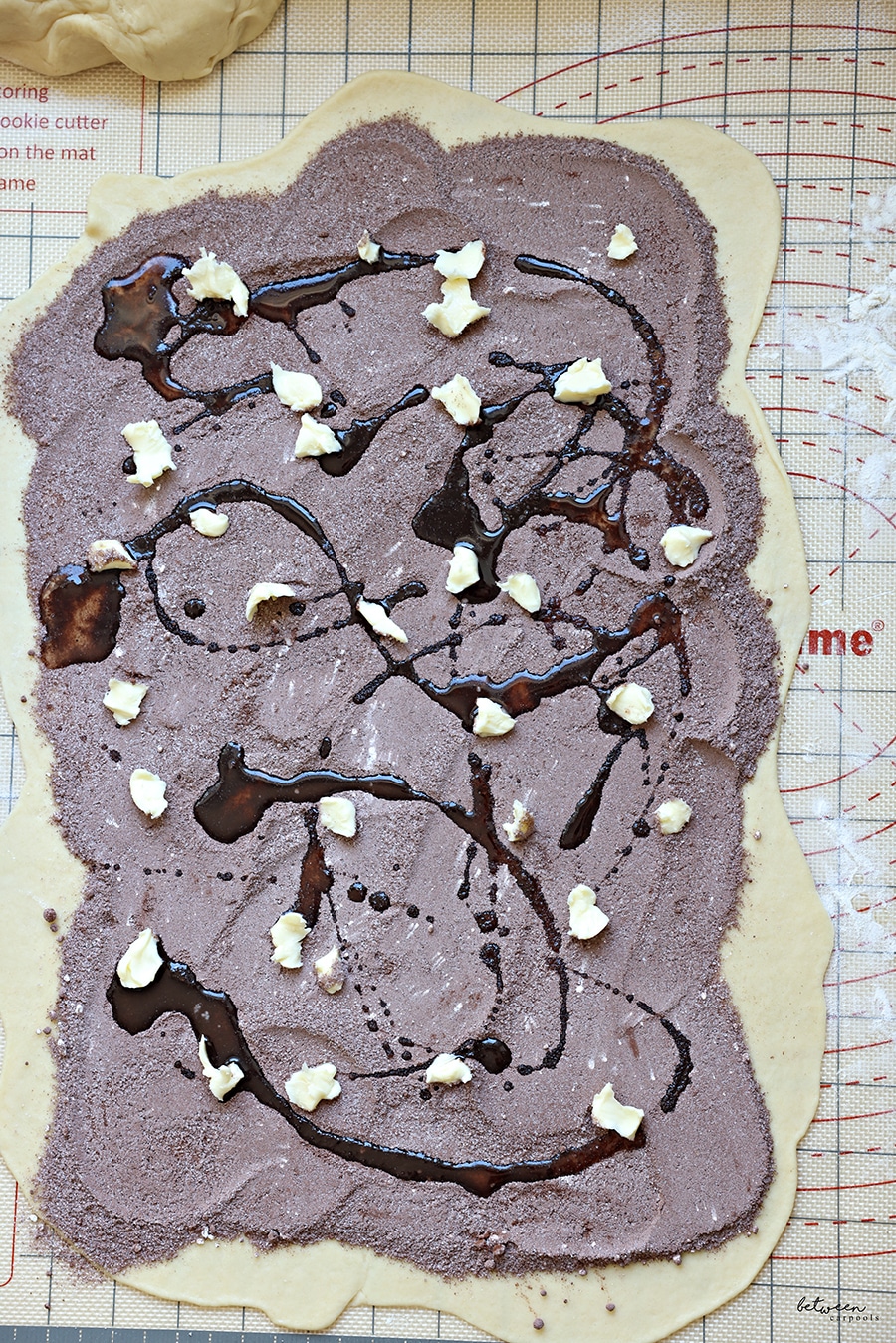 a drizzle of oil on dots of butter scattered across rolled kokosh dough sprinkled with cocoa + sugars