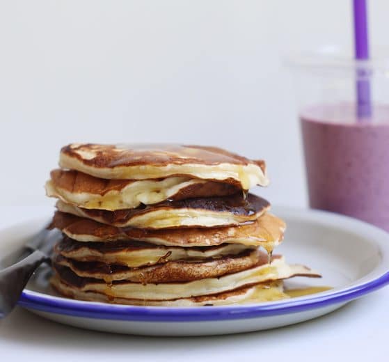 A stack of protein pancakes on a plate, and a fruit smoothie.
