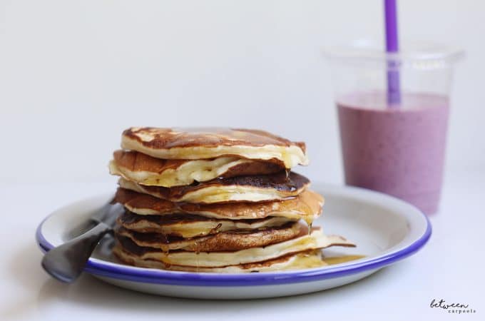A stack of protein pancakes on a plate, and a fruit smoothie.