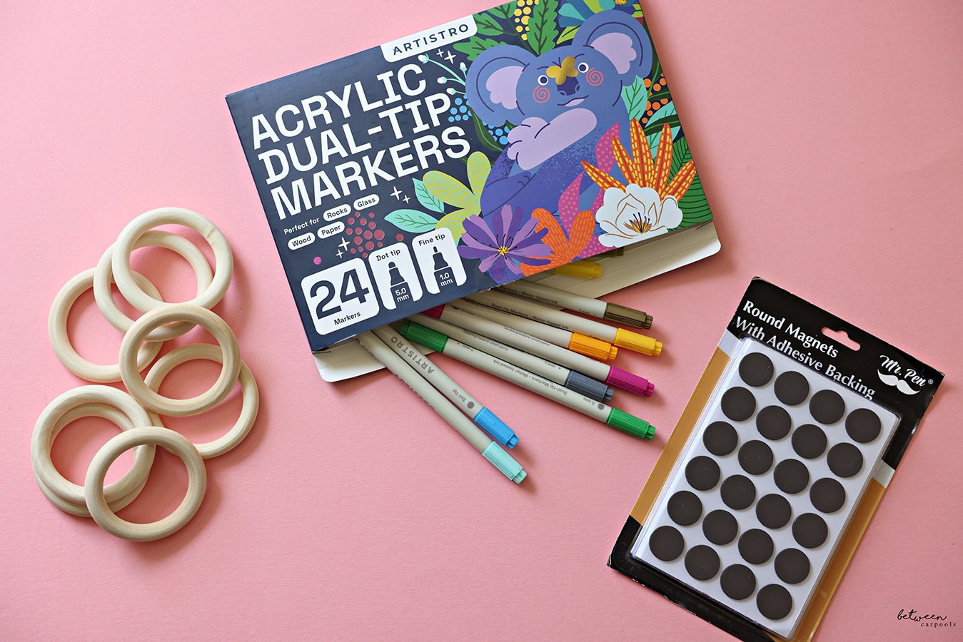 wooden rings, paint markers, and magnet on pink background