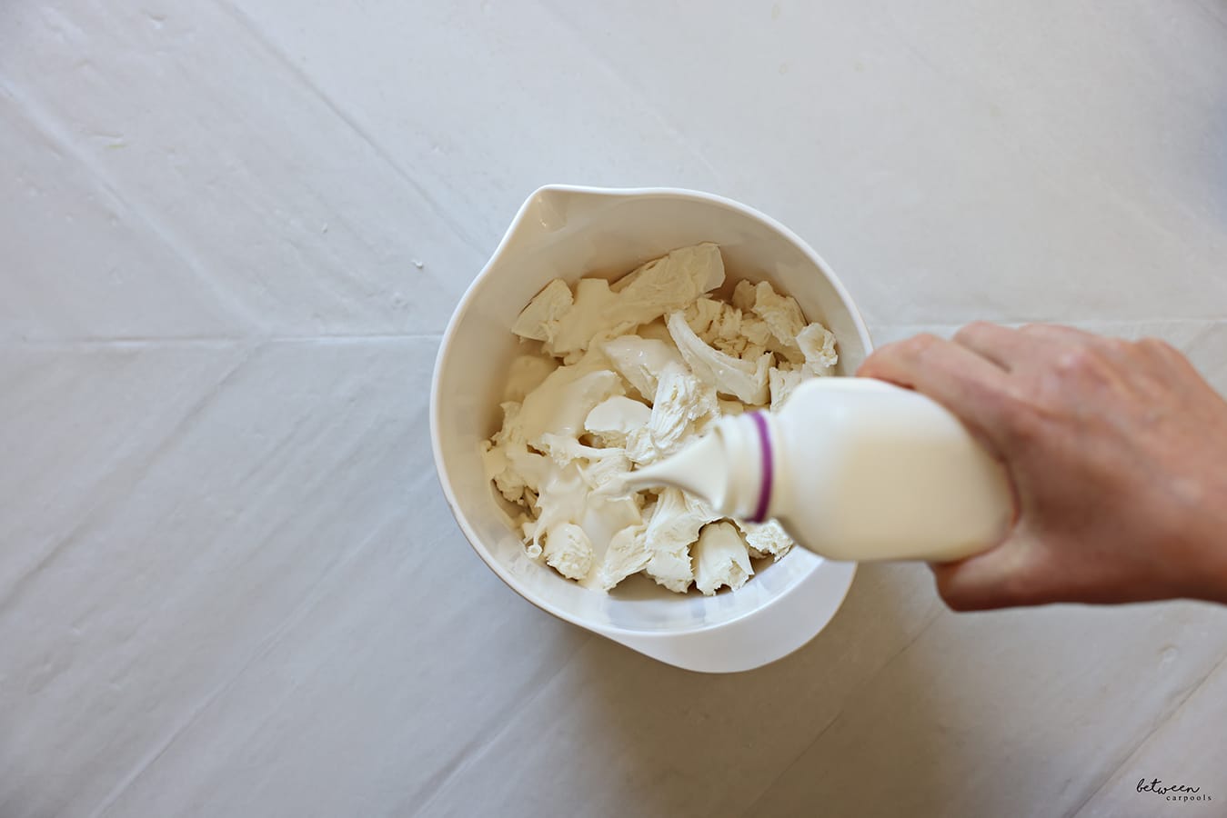 adding heavy cream and salt to shredded fresh mozzarella cheese in a spouted mixing bowl